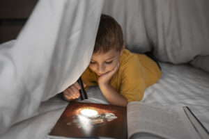 front-view-kid-reading-magazine-with-flashlight