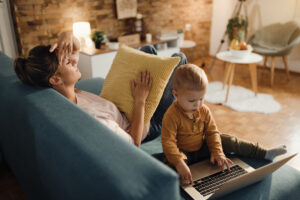 Small boy using laptop while his mother is trying to relax at ho
