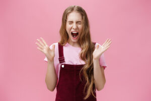Young girl scared to death seeing spider in room yelling out loud closing eyes and opening mouth gesturing with raised hands near chest feeling afraid and insecure posing against pink background
