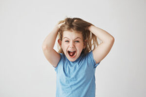 Beautiful little girl with light hair screaming loudly, holding hair with hands, being scared with big spider on the wall in bedroom.