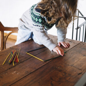girl-forming-square-shape-with-plastic-sticks-wooden-desk